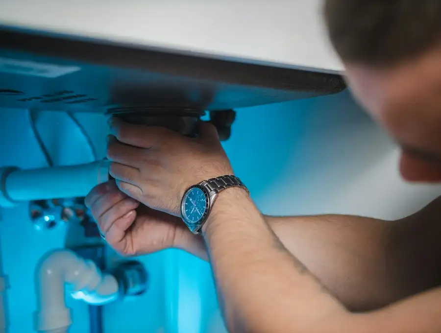 Installateur schraubt an einem Anschluss unter dem Waschbecken