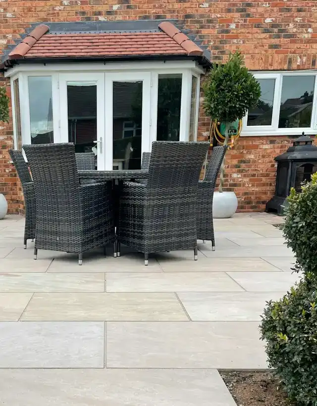 Terrasse aus hellen Natursteinplatten mit Gartenmöbeln