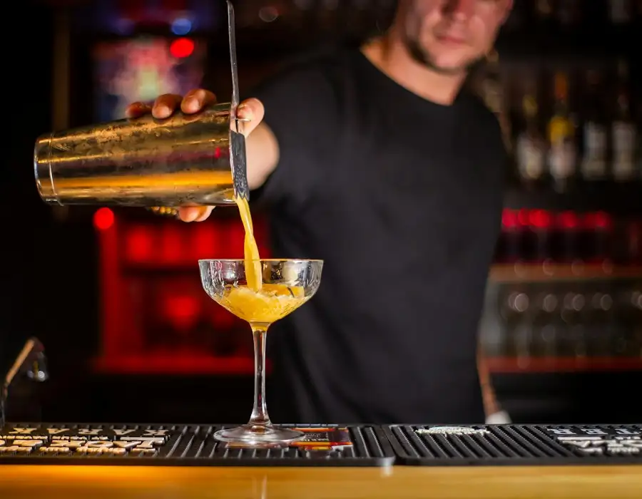 Bartender gießt einen Cocktail aus dem Shaker in eine Coupette