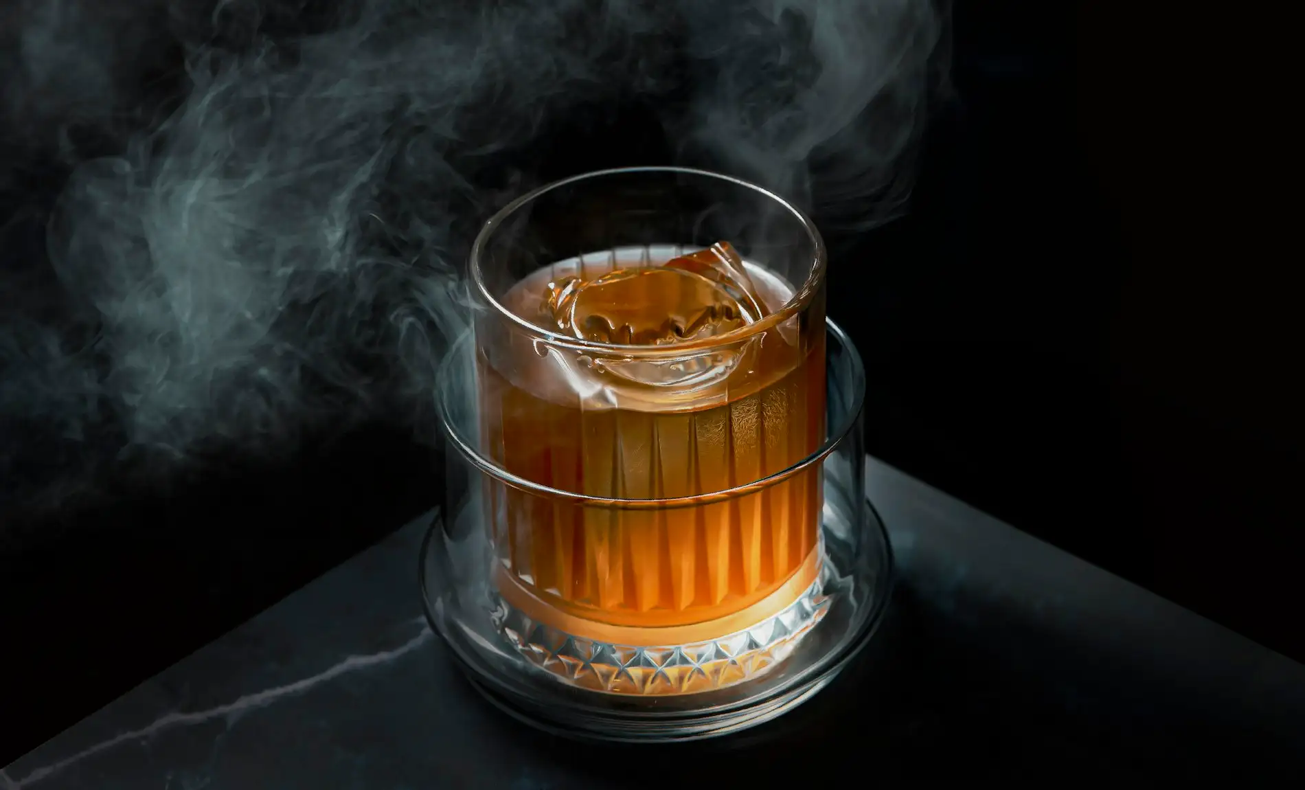 Cocktail im Tumbler unter einer Rauchwolke auf dunklem Tresen