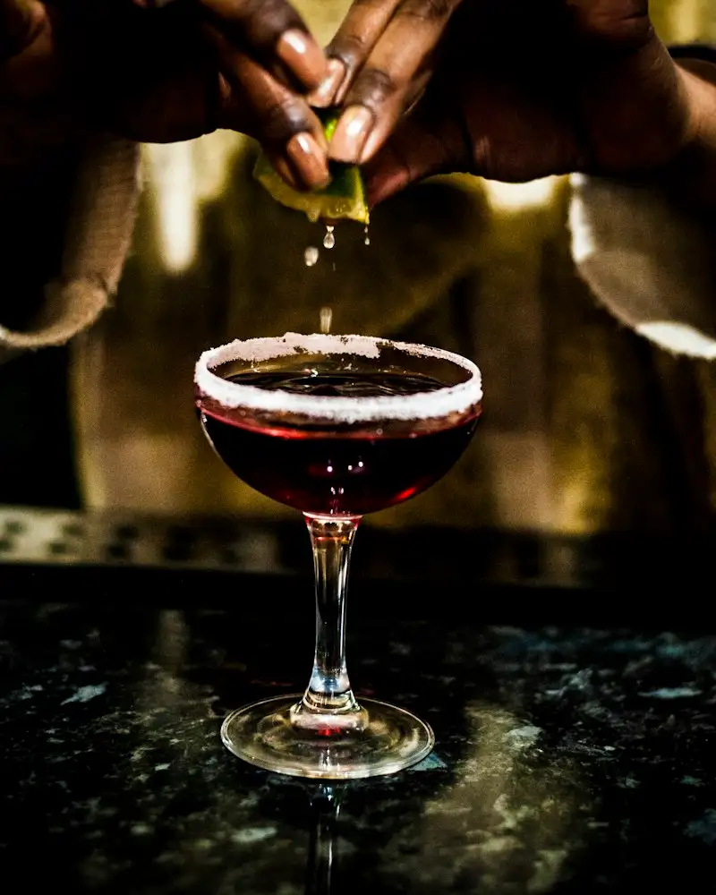 Bartender presst Limette über einem Cocktail mit Zuckerrand