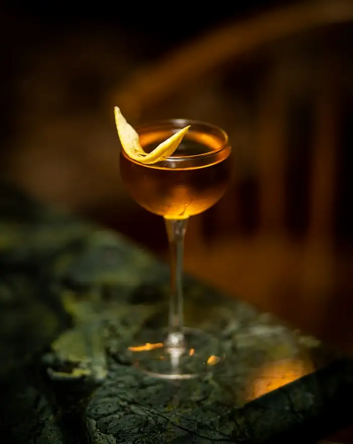 Bernsteinfarbener Cocktail in einer Coupette mit Zitronenzeste