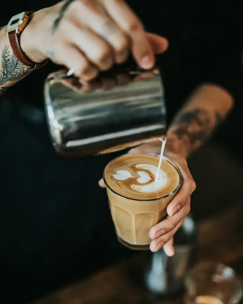 Barista gießt Milchschaum in einen Becher